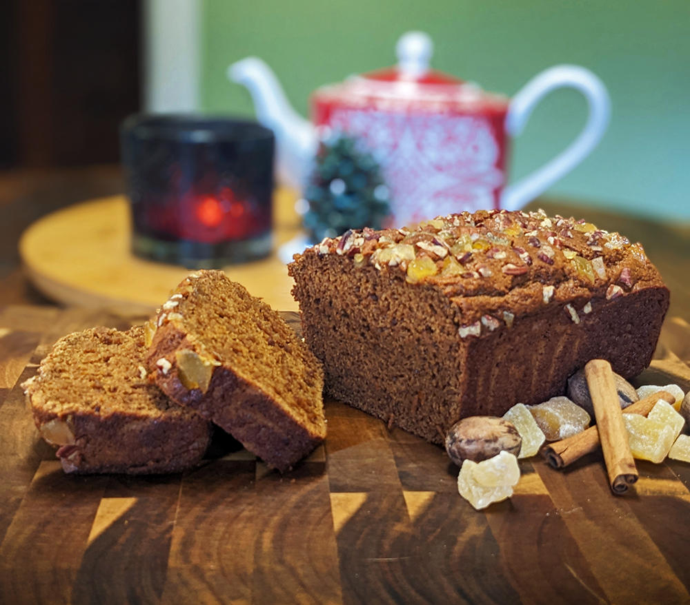 A gingerbread loaf sits on a wooden cutting board with two slices.
